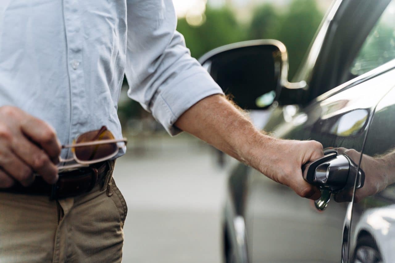 The senior man opens the door of his car with keyless access.