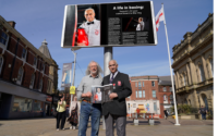 Yaqoob Hussain and Leader of the Council Phil Riley holding the Shuttle magazine outside Blackburn Town Hall digital screen