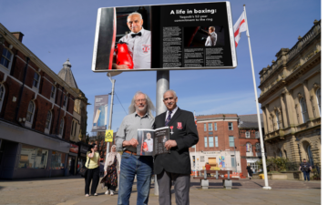 Yaqoob Hussain and Leader of the Council Phil Riley holding the Shuttle magazine outside Blackburn Town Hall digital screen